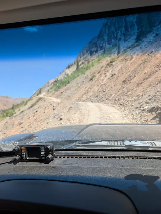 A dashboard-mounted radio with a narrow rocky trail winding along a mountainside ahead.