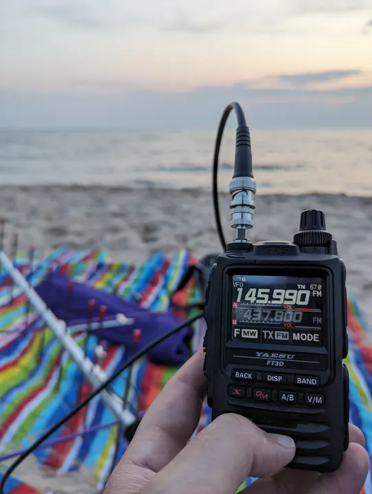 A handheld radio at a beach, with colorful folding chairs, calm water, and evening clouds.