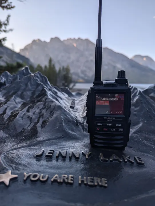 A handheld radio standing on a raised-relief mountain map, with real peaks visible behind.