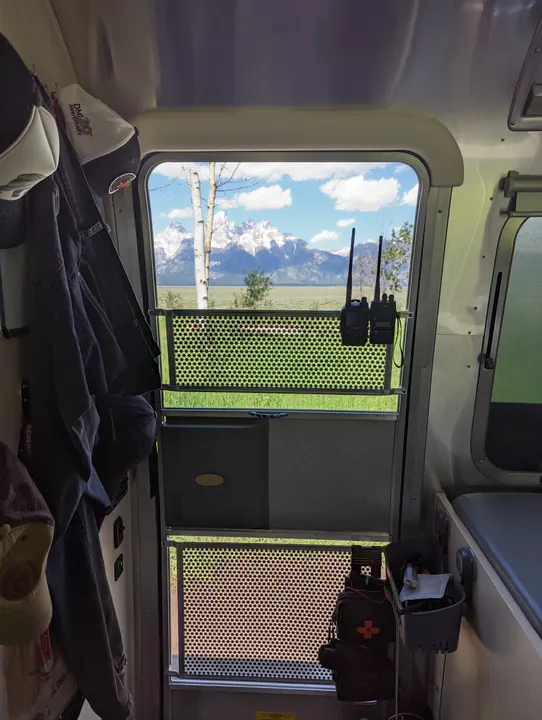 Handheld radios hanging by a camper screen door, with a mountain view outside.