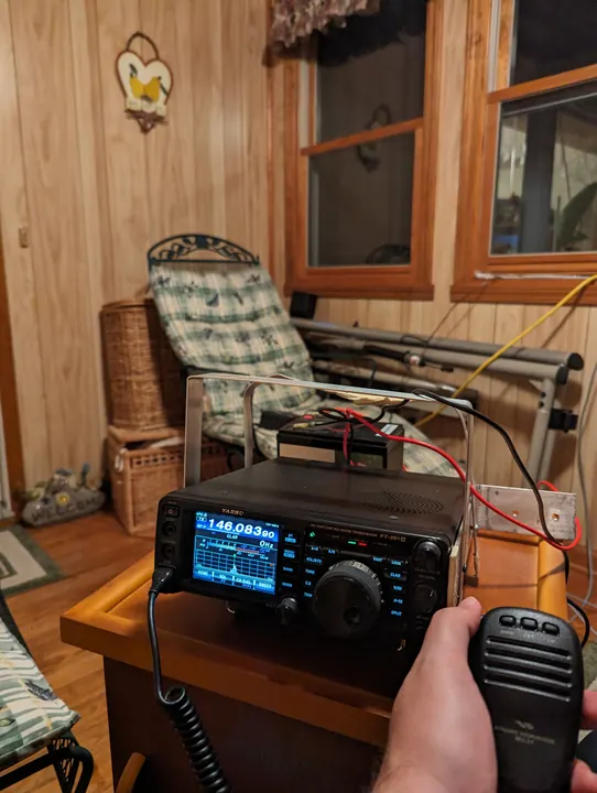 A portable radio, battery, and microphone on a table in a wood-paneled cabin.