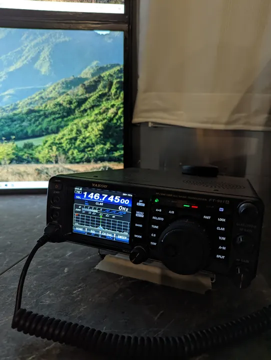 A portable radio and microphone inside a camper, with a green mountainside visible through the window.