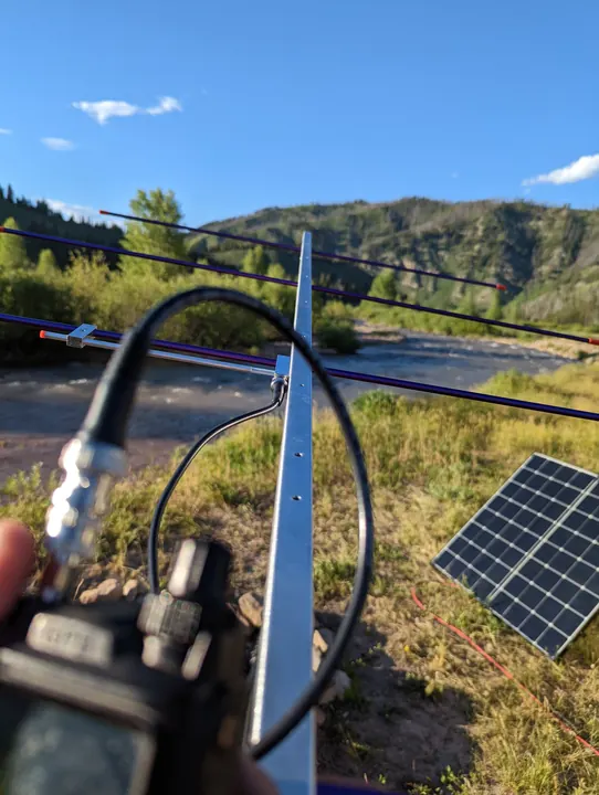 A portable directional antenna and radio at a campsite with a solar panel and wooded hills.