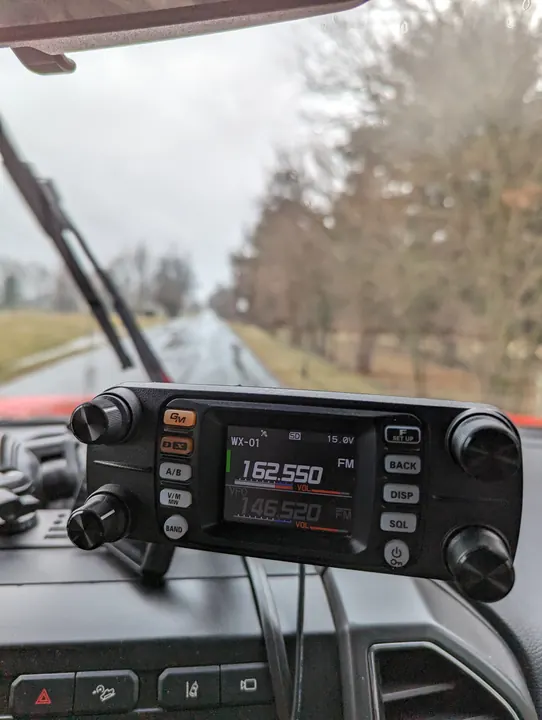 A vehicle-mounted radio on the dashboard, looking out onto a quiet road lined with trees.