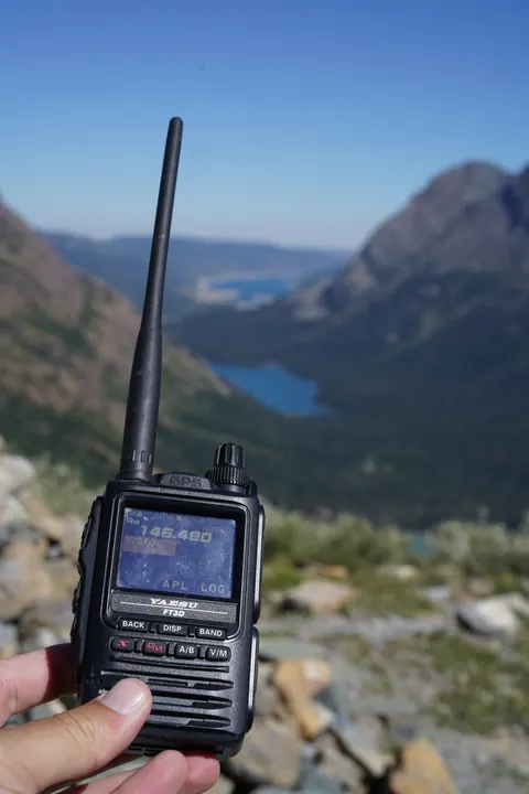 A handheld radio above a blue mountain lake, with steep peaks in the distance.